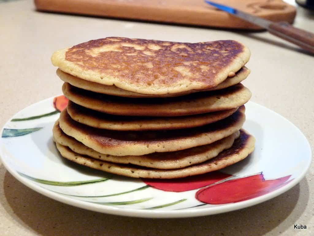 Stos puszystych amerykańskich pancakes polanych syropem klonowym na białym talerzu